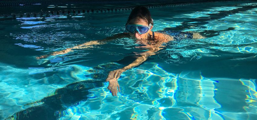 The child swims comfortably because the pool heat pump is running to keep the pool water warm despite the cold weather.