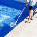 The man is cleaning the pool.